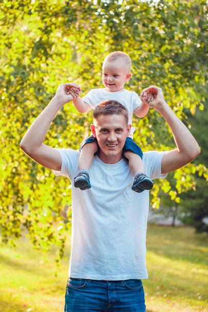 Father holding his son on shoulders in park - Foto, afbeelding