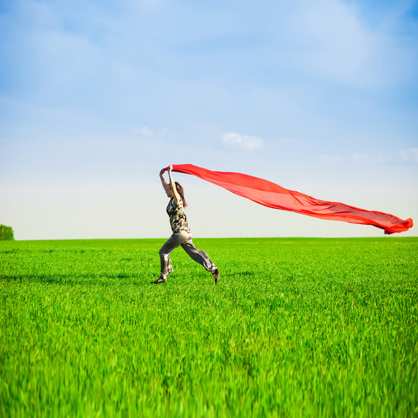 Красивая молодая женщина прыгает по зеленому лугу с цветной тканью
 - Фото, изображение