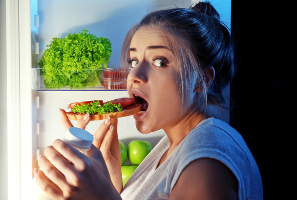 Beautiful girl eating sandwich at night. Unhealthy food concept - Photo, Image