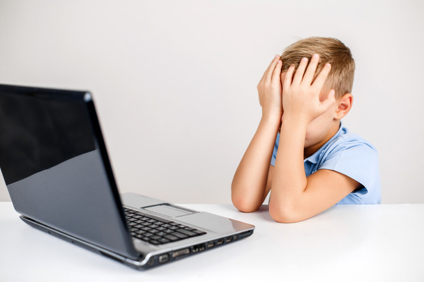 Scared kid covering his face at desk with laptop - Foto, immagini