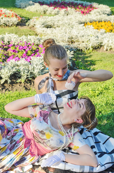 Two retro-style girls on a summer picnic reading a book aloud - Photo, Image