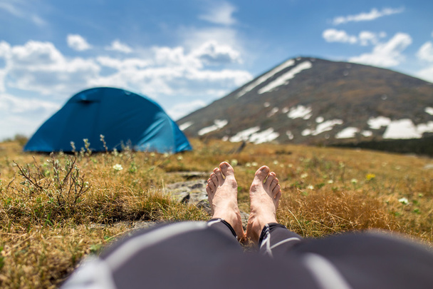 bare feet of resting camper with tent and mountain view at backg - Photo, Image