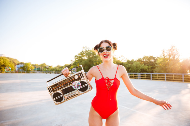 Girl in sunglasses and red swimsuit holding old record player - Foto, afbeelding