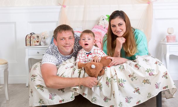 Portrait of cheerful family lying with 1 year old son on bed - Foto, afbeelding
