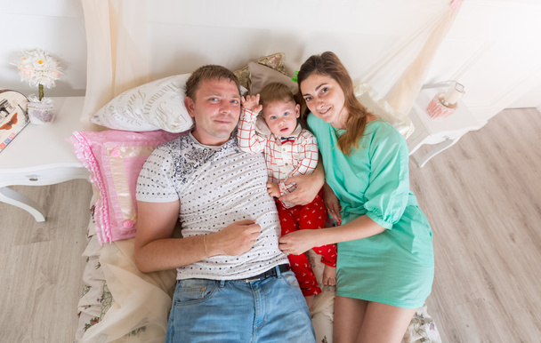 Bovenaanzicht portret van familie met babyjongen op bed liggen - Foto, afbeelding