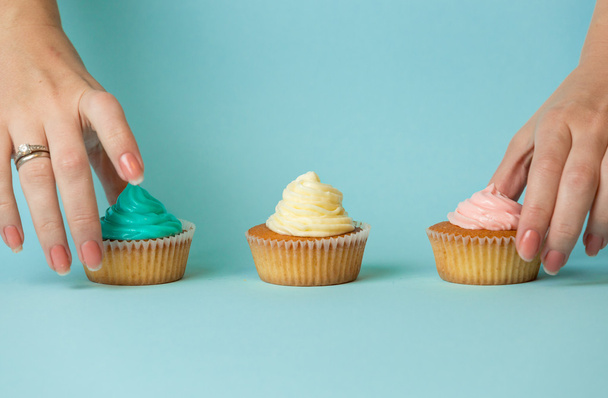 Close-up van vrouwelijke handen kiezen tussen drie kleurrijke cupcakes - Foto, afbeelding