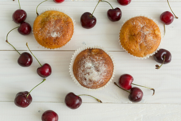 Tre muffin e ciliegie sul tavolo di legno bianco
 - Foto, immagini