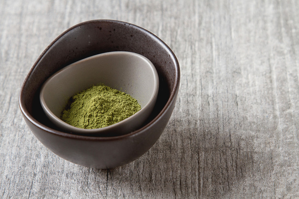 Dry Matcha tea in a small brown plate. Grey wood background - Foto, immagini