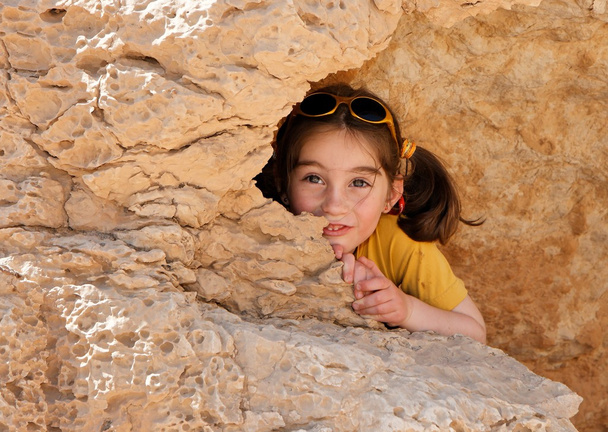 Милая маленькая девочка прячется за скалой
 - Фото, изображение