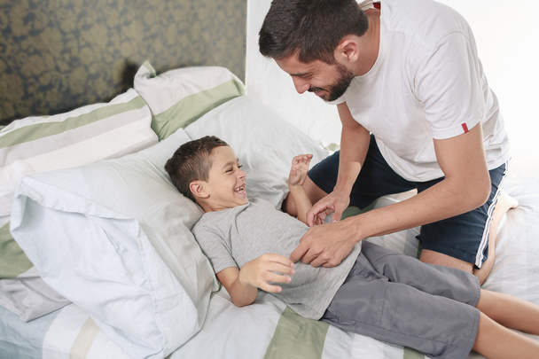 Father tickling his son on the bed - Фото, изображение
