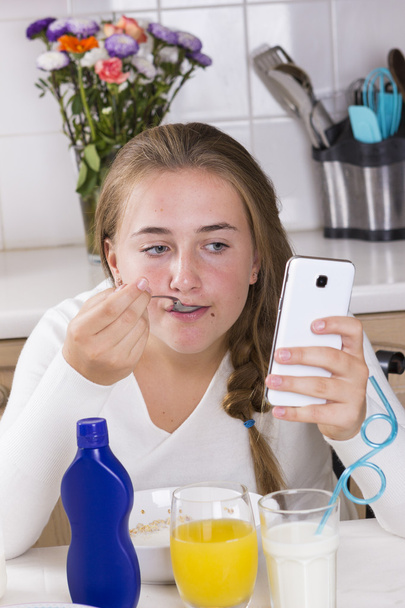 Девушка с телефоном завтракает на кухне
 - Фото, изображение