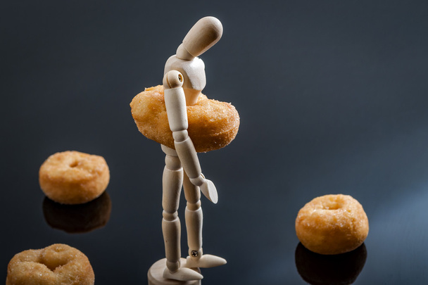 Human shaped figurine surrounded by doughnuts and with a doughnut around the waist made to look like the belly of a overweight person - Photo, Image