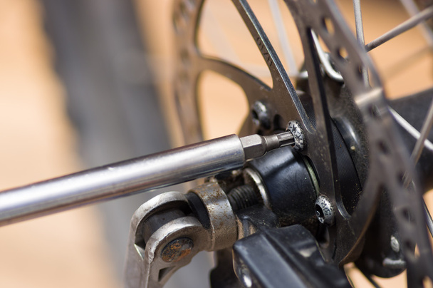 Lähikuva multi ruuvimeisseli työskentelevät mekaaniset osat vieressä pyörän pinnoja
 - Valokuva, kuva