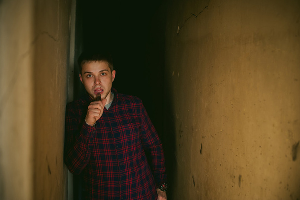 man in a plaid shirt and jeans, smokes an electronic cigarette, blowing smoke and steam from the vaporization a mechanical device. location Abandoned unfinished building, brick walls, stylish. - Фото, зображення