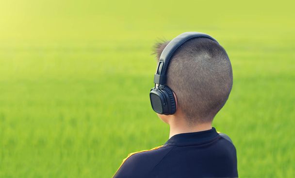  Menino com cabeça de pele ouvindo música por fone de ouvido sem fio no campo
 - Foto, Imagem