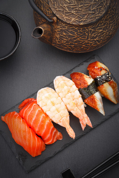 Sushi nigiri set on a stone plate over black background - Foto, afbeelding