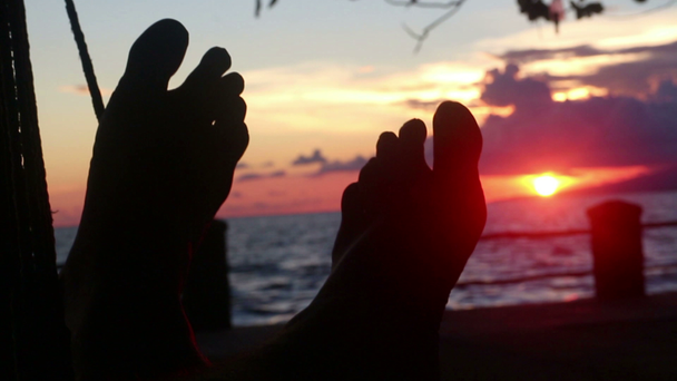 cu Silhouette der Füße in der Hängematte mit tiefrotem Sonnenuntergang und Meer - Filmmaterial, Video