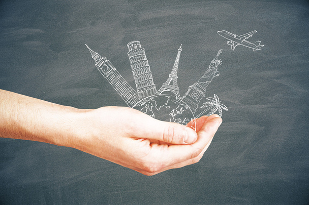 Male hand holding abstract sketch of landmarks and airplane on chalkboard background. Travel concept - Valokuva, kuva