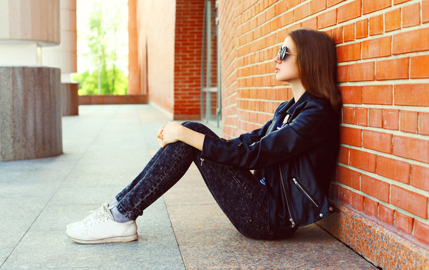 Fashion woman in black rock style sitting over bricks background - 写真・画像