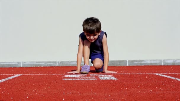Mały chłopiec przygotowania do uruchomienia w athletic toru - Materiał filmowy, wideo