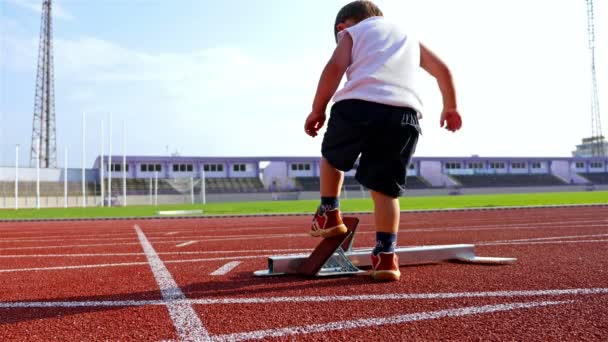 Grappige video van een 2 jaar oude jongen voorbereiden om sprint vanuit een startblok - Video
