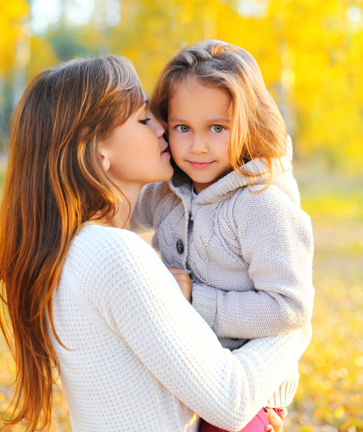 Portrait happy mother kissing child in warm sunny autumn day - Photo, image