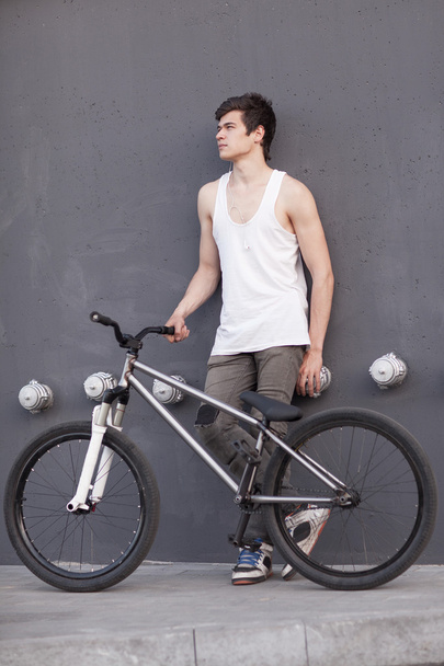 Boy with silver bike stay at grey wall background - Φωτογραφία, εικόνα