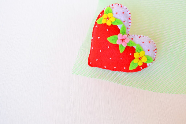 Hand gemaakte voelde hart. Symbool van de dag van Valentijnskaarten. Mooi hart handgemaakt op groene en witte achtergrond - Foto, afbeelding