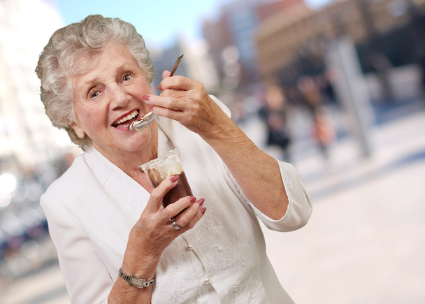 Портрет пожилой женщины, кушающей шоколад и крем на улице
 - Фото, изображение