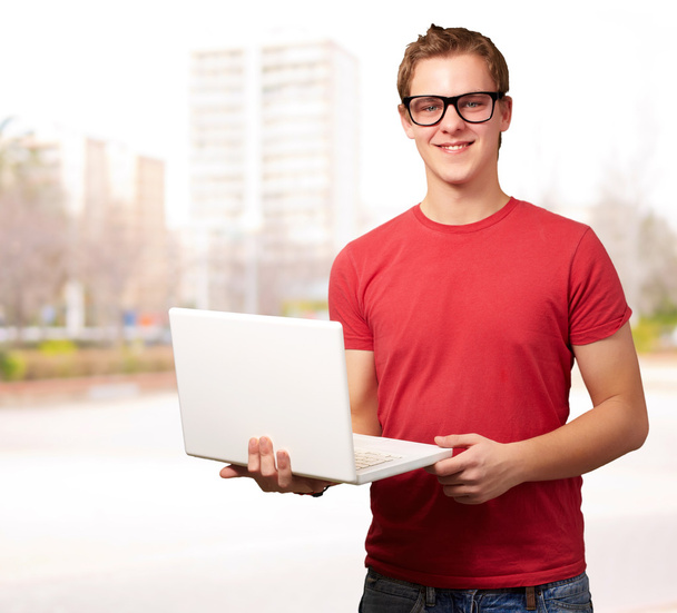 Porträt eines jungen Studenten mit Laptop vor einem Stadtbild - Foto, Bild