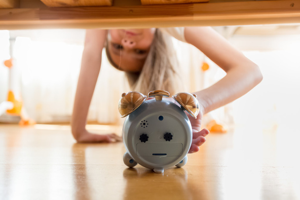 Portrait of girl reaching for alarm clock under the bed - Photo, Image