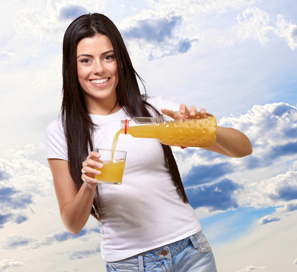 Portret van een jonge vrouw een sinaasappelsap in een glas gieten - Foto, afbeelding