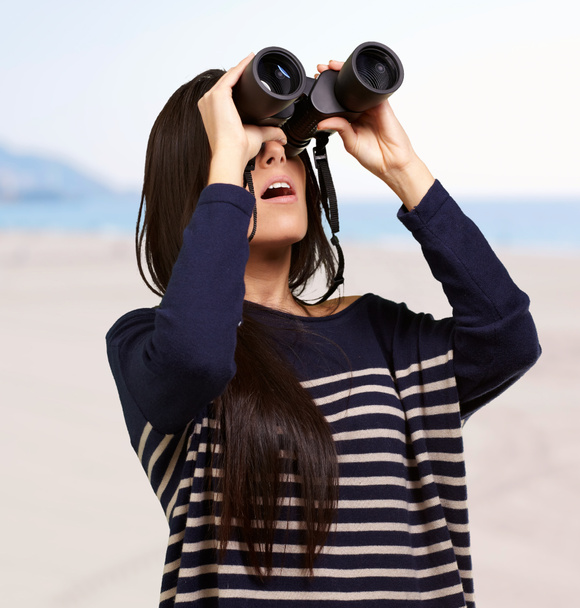 Portrait of young woman looking through a binoculars against a b - Photo, Image