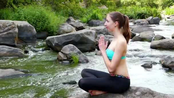 Giovane e bella ragazza sta meditando sulla roccia. Respira profondamente l'aria fresca di un fiume di montagna
. - Filmati, video