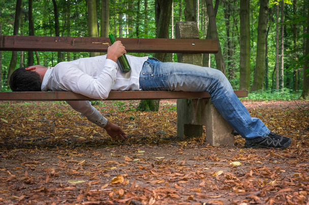 Homem bêbado dormindo em um banco de parque com garrafas de cerveja
 - Foto, Imagem