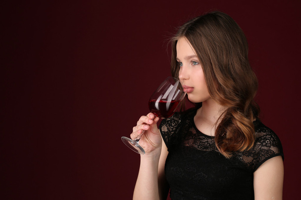 Girl touching wineglass by her lips. Close up. Dark red background - Photo, Image