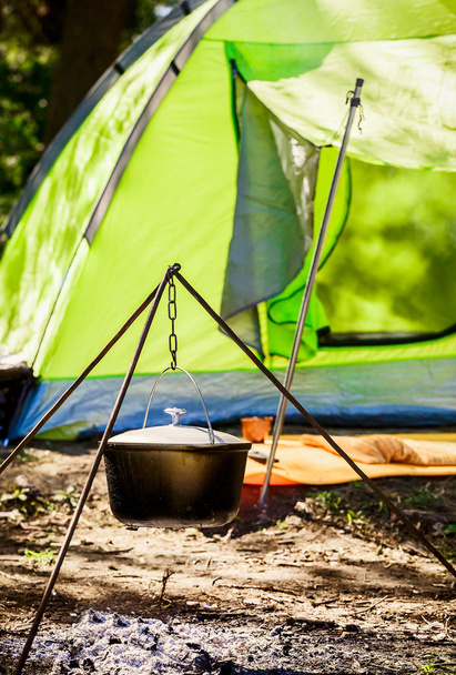 a pot hanging on a tripod on the background of the tent. Cooking over a campfire on the nature - Photo, Image