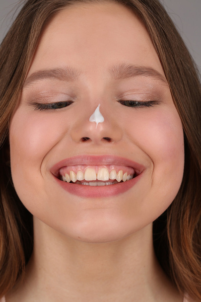 Model with cream on her nose. Close up. Gray background - Фото, изображение