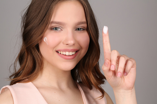 Lady with cream showing one finger. Close up. Gray background - Photo, image