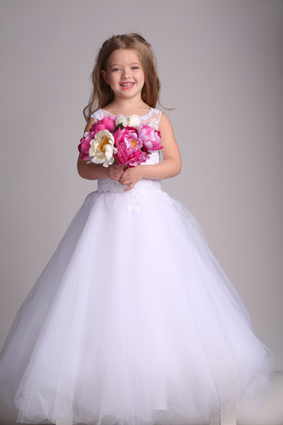 Little girl in wedding dress with bunch of flowers. Gray background - Foto, Imagen