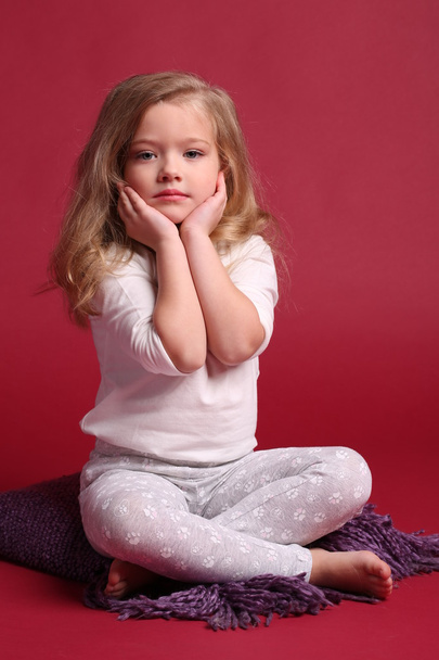 Baby in pajamas touching her cheeks. Red background - Foto, imagen