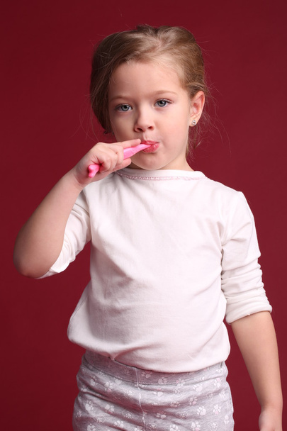 Little girl brushing her teeth. Close up. Red background - Foto, immagini