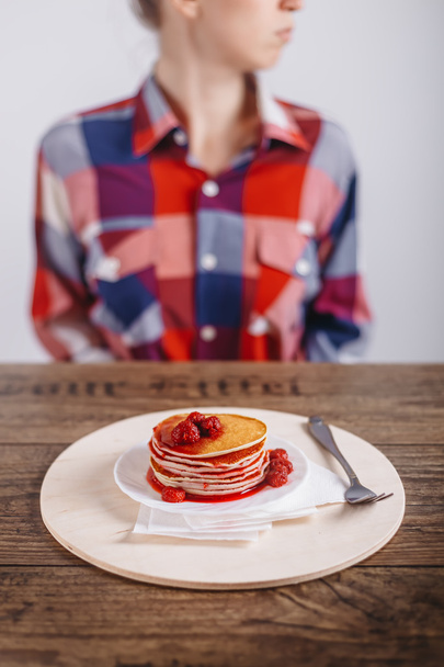 American Pancakes with raspberry jam on a wooden table, woman in the background, food advertising concept. Closeup, selected focus. - Fotografie, Obrázek