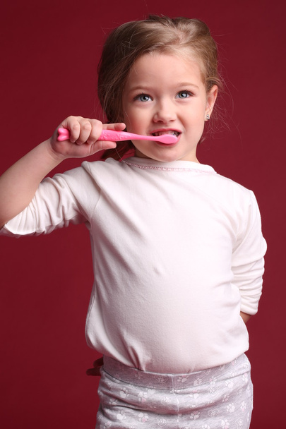 Baby brushing her teeth. Close up. Red background - Photo, Image