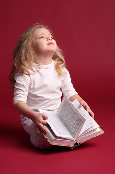 Criança sentada em roupa de dormir com um livro. Fundo vermelho
 - Foto, Imagem