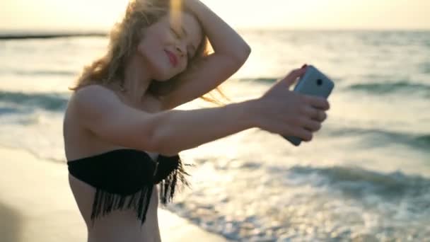 Young beautiful girl with red lips in swimwear smiling, making selfie at seaside - 映像、動画