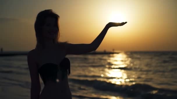 Σιλουέτα του όμορφη κοπέλα με μαγιό κρατώντας ήλιο στο seaside στο sunrise - Πλάνα, βίντεο