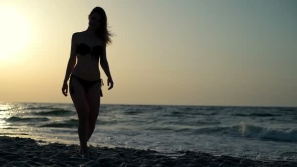 Sziluettjét a fiatal gyönyörű lány fürdőruha mosolyogva, séta a tengerparton - Felvétel, videó