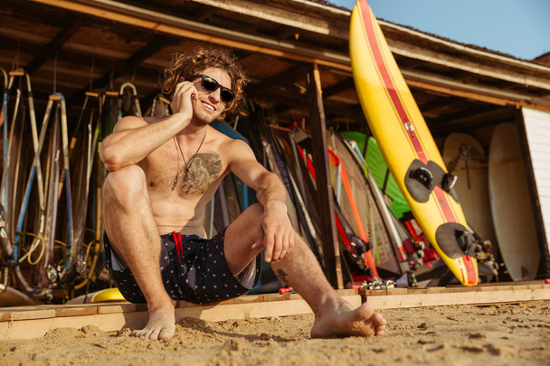 Surfeur homme à lunettes assis et parlant sur smartphone à l'extérieur
 - Photo, image