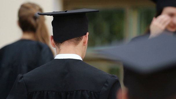 Jóvenes alegres con vestidos y gorras académicas listos para la ceremonia de graduación
 - Imágenes, Vídeo